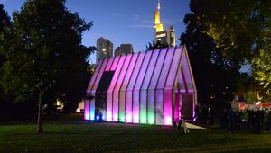 Die Lichtkirche bei Nacht. Die Hülle des Gebäudes erstrahlt in lila und bunten Farben.